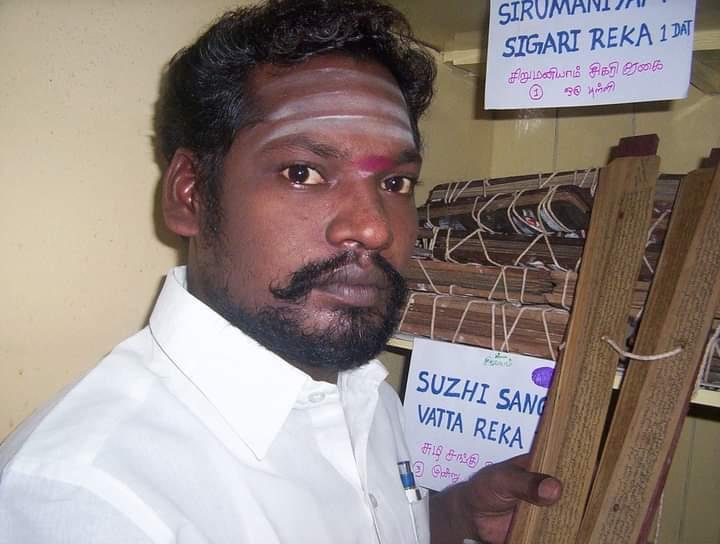 Guruji beside shelves of catalogued olai chuvadi palm-leaf bundles